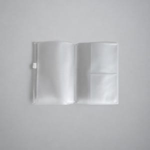 May include: A clear, translucent plastic passport holder or document cover laid open flat. The cover features a small white tab on the left side and interior pockets on the right side designed for holding cards or identification documents securely.