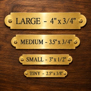 May include: Four rectangular brass plaques with rounded ends and screw holes, each engraved with black text. The sizes are labeled as LARGE - 4" x 3/4", MEDIUM - 3.5" x 3/4", SMALL - 3" x 1/2", and TINY - 2.5" x 3/8". Each plaque features a metallic finish.