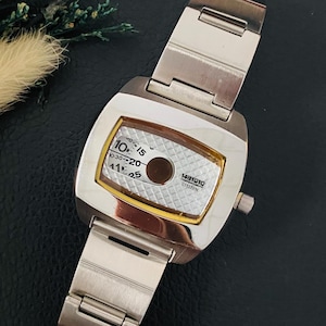May include: A silver-toned Citizen wristwatch with a rectangular case and a metal link bracelet. The watch face features a white textured background with black numerical markings, a circular dark center, and a gold-colored inner bezel frame.