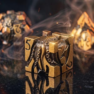 May include: A metallic gold-toned six-sided die featuring a detailed octopus relief design with tentacles wrapping around the faces. The number five is clearly engraved on the top corner, while other numbers are visible on the sides.