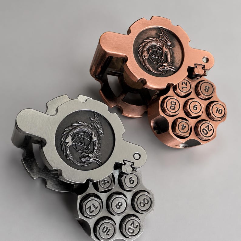 May include: Two metal dice holders shaped like revolver cylinders with a gear-like top featuring an embossed dragon encircling a twenty-sided die. One holder is copper-toned, and the other is silver-toned. Each cylinder has slots for dice labelled with numbers.