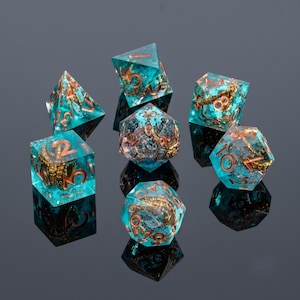 May include: A set of seven polyhedral dice made of translucent teal resin, each containing a miniature gold-colored octopus tentacle. The numbers on the dice are etched in a metallic copper color, providing a clear contrast against the blue-green material.