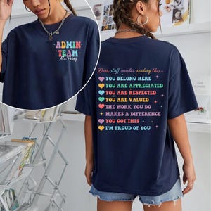 May include: Navy blue t-shirt with the text "ADMIN TEAM Ms. Perez" on the front. The back of the shirt has a colorful message: "Dear staff member reading this... You belong here, You are appreciated, You are respected, You are valued..."