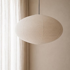 May include: A large, oval-shaped pendant lamp featuring a cream-colored paper shade with horizontal ribbed detailing. The light fixture is suspended from the ceiling by a thin, black cord, creating a soft and diffused lighting effect.