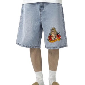 May include: Light blue denim shorts with a relaxed fit. The shorts feature a colorful graphic on the right leg with praying hands, roses, and the text "TRUST THE PROCESS". The shorts are worn with a white t-shirt, white socks, and brown suede slip-on shoes.