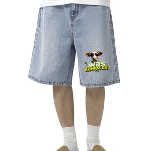 May include: Light blue denim shorts with a humorous graphic of a cow wearing sunglasses and the text "Was KUHgst du?" printed on the right leg. The shorts have a relaxed fit and a classic five-pocket design.
