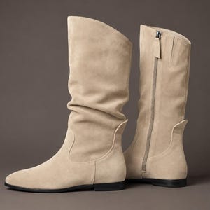 Peut inclure: Une paire de bottes mi-mollet beige avec une tige souple et plissée, un bout arrondi et une semelle plate noire. Les bottes sont dotées d'une fermeture éclair latérale qui s'étend du haut de la tige jusqu'à la zone de la cheville.