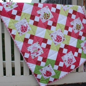 May include: A pink, green, and white patchwork quilt with a repeating pattern of squares and a small floral print. The quilt features a whimsical design of a bird with a red beak and a green body.