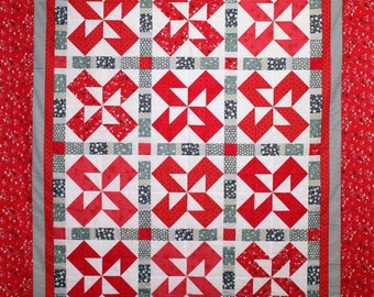 May include: A red and white quilt with a geometric pattern. The quilt is made up of squares with a starburst design in the center. The quilt is bordered with a red and white striped fabric.