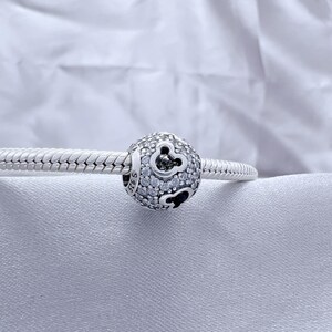 May include: A spherical silver charm bead featuring a pavé setting of clear cubic zirconia stones and cutout mouse ear silhouettes. The charm is threaded onto a silver snake chain bracelet, with the hallmark S925 visible on the side of the bead.
