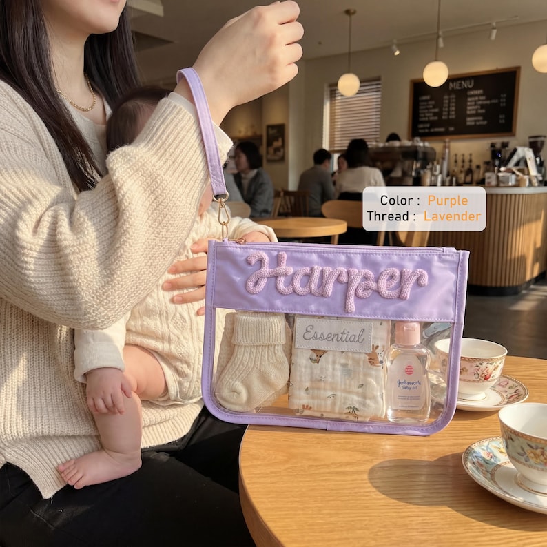 May include: A rectangular lavender pouch with a clear front panel and a wrist strap. The name Harper is embroidered in lavender thread on the front. Inside the pouch are a pair of cream-colored knit socks, a patterned cloth, and a small bottle.