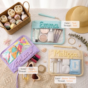 May include: Three rectangular clear cosmetic pouches with wrist straps, featuring embroidered names. One teal pouch labeled Emma, one purple pouch labeled Harper, and one butter yellow pouch labeled Melissa. Each contains various personal care items.
