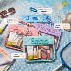 May include: Four rectangular clear pouches with wrist straps, each featuring a personalized name in textured embroidery. The pouches come in sky blue, pink, purple, and teal, containing various skincare and cosmetic items like tubes and brushes.