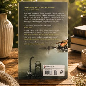 May include: The back cover of a book titled "Man's Search for Meaning" by Viktor Frankl, with quotes from The New York Times and other authors. The book is set on a wooden surface with a vase of flowers and a cup.