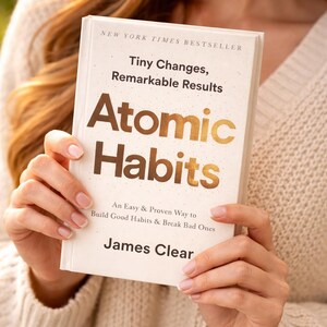 May include: A hardcover book titled "Atomic Habits" by James Clear. The book has a white cover with gold lettering and the text "Tiny Changes, Remarkable Results." The book is a New York Times bestseller and promises an easy way to build good habits and break bad ones.