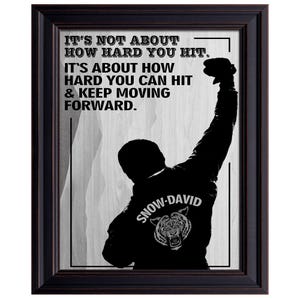 May include: Framed black and white print featuring a silhouette of a person with their fist raised. The print includes the text "IT'S NOT ABOUT HOW HARD YOU HIT. IT'S ABOUT HOW HARD YOU CAN HIT & KEEP MOVING FORWARD." The back of the jacket says "SNOW-DAVID".