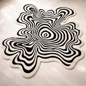 May include: A black and white rug with a unique, abstract design. The rug features a swirling pattern of black lines against a white background, creating a visually striking effect. The rug's shape is irregular, adding to its artistic appeal. This decorative rug is suitable for any room.