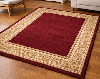 Puede incluir: Una alfombra rectangular con un centro rojo intenso y un borde beige con un patrón floral ornamentado y repetitivo. La alfombra está colocada sobre un suelo de madera, creando un ambiente cálido y acogedor.