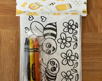 May include: A coloring activity set featuring a white card with black line art of two bees and three flowers. Three Crayola crayons in blue, yellow, and orange are included in a clear plastic sleeve. The set has a decorative header with honey pots.