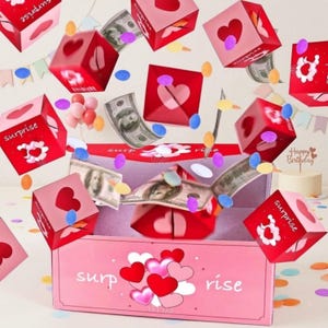 May include: A pink box with the word "surprise" and "rise" printed on it, surrounded by red heart-shaped boxes and dollar bills. The boxes have heart cutouts and the word "surprise" printed on them. Confetti and a small cake are also visible.