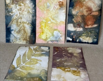 May include: Five rectangular art prints featuring botanical eco-prints. The top left shows a dark blue background with a golden fern leaf. The top centre is pink and yellow. The top right displays orange flowers on dark blue. Bottom prints show yellow leaves and dark purple foliage.