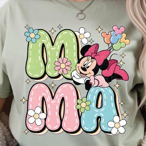 Puede incluir: Camiseta verde claro con la palabra "MAMA" en letras grandes y coloridas. La "M" es verde, la "A" es rosa, la "M" es rosa y la "A" es azul. Minnie Mouse aparece en el dise&ntilde;o, sosteniendo globos.