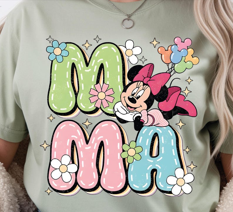 Puede incluir: Camiseta verde claro con la palabra "MAMA" en letras grandes y coloridas. La "M" es verde, la "A" es rosa, la "M" es rosa y la "A" es azul. Minnie Mouse aparece en el dise&ntilde;o, sosteniendo globos.