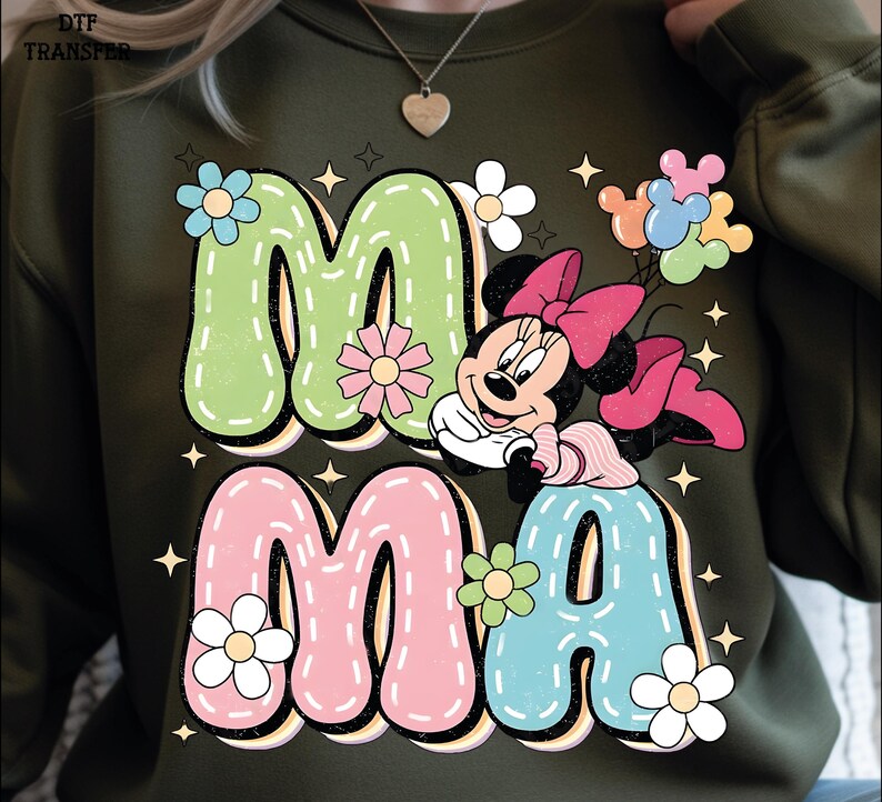 Puede incluir: Sudadera verde oliva con la palabra "MAMA" en letras grandes y coloridas con una fuente retro. El dise&ntilde;o incluye a Minnie Mouse, flores y estrellas. Las letras est&aacute;n delineadas en blanco y tienen un efecto cosido.