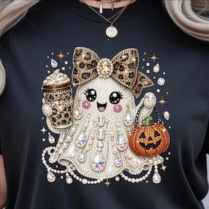 May include: A black t-shirt featuring a graphic of a white ghost adorned with sparkling rhinestones and pearls. The ghost wears a leopard print bow, holds a coffee cup with a leopard print sleeve, and carries an orange jack-o'-lantern bucket.