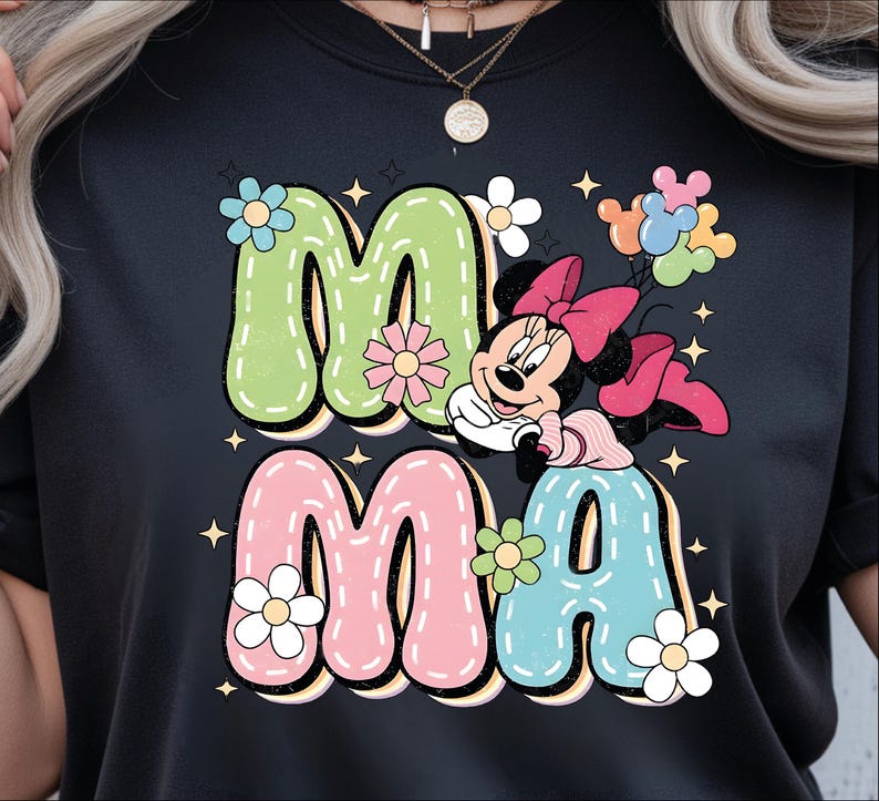 Puede incluir: Camiseta negra con la palabra "MAMA" en colores pastel y una fuente retro. Minnie Mouse se representa con un lazo rosa y globos. Acentos florales y estrellas rodean el texto, creando un dise&ntilde;o alegre.
