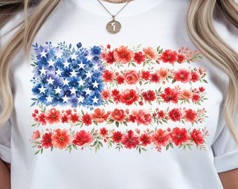May include: White t-shirt featuring a floral American flag design. The flag's stars are composed of blue flowers, and the stripes are made of red flowers. The shirt is a crew neck and has short sleeves.
