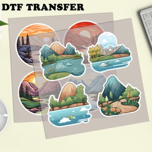 Puede incluir: Una hoja de pegatinas de transferencia DTF con dise&ntilde;os de paisajes. Cada pegatina presenta monta&ntilde;as, agua, &aacute;rboles y puestas de sol en colores vibrantes. Las pegatinas est&aacute;n sobre un fondo gris claro. El texto 'DTF TRANSFER' est&aacute; en la parte superior.