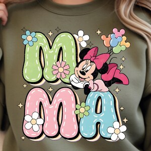 Puede incluir: Sudadera verde oliva con la palabra "MAMA" en letras grandes y coloridas. La "M" es verde, la "A" es azul y las otras "M" y "A" son rosas. Minnie Mouse aparece en el dise&ntilde;o, sosteniendo globos y rodeada de flores y estrellas.