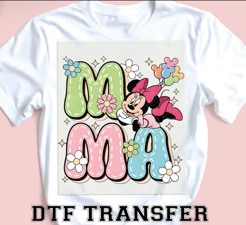 Puede incluir: Camiseta blanca con un gr&aacute;fico colorido. La palabra "MAMA" est&aacute; en letras de burbujas, decorada con flores y un personaje de dibujos animados sosteniendo globos. El texto "DTF TRANSFER" est&aacute; impreso en la parte inferior.
