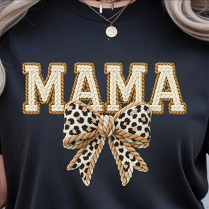 May include: Black t-shirt with the word "MAMA" in a white and brown rope design. A leopard print bow is centered below the word. The shirt is a crew neck style.
