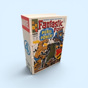 Peut inclure: Une boîte rectangulaire en bois présentant une couverture imprimée d'une bande dessinée vintage Fantastic Four intitulée The Peril and the Power. Le panneau latéral affiche le logo Marvel, un symbole quatre bleu et le texte MAR.