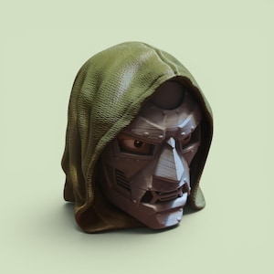 Op de afbeelding: Een driedimensionale buste van een personage met een textuurrijke olijfgroene capuchon en een metaalgrijs gezichtsmasker. Het masker heeft een stijf, hoekig ontwerp met zichtbare klinknagels, een opvallende neus en horizontale ventilatieopeningen.