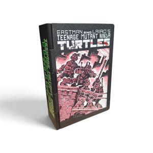 May include: A black rectangular video game cartridge featuring the title Eastman and Laird's Teenage Mutant Ninja Turtles in white text. The front label displays a red and black graphic illustration of four turtle characters on a rooftop.