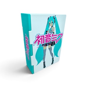 Può includere: Un raccoglitore bianco e turchese con un'illustrazione grafica del personaggio Hatsune Miku con lunghi capelli turchesi. La copertina mostra il personaggio accanto al testo giapponese rosa 初音ミク e al testo inglese HATSUNE MIKU.