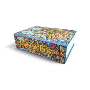 May include: A rectangular storage box featuring a vibrant, multi-coloured graphic pattern with blue, yellow, and red tones. The front panel displays the text "Odds and Ends" in a bold, yellow font against a detailed, intricate illustrated background.