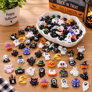 May include: A collection of small, colorful Halloween-themed resin cabochons featuring ghosts, pumpkins, bats, haunted houses, and moons. These miniature decorative pieces are scattered across a surface, with many contained in a white scalloped bowl.