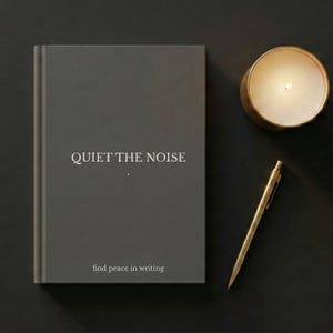 Puede incluir: Un diario gris oscuro con el texto "QUIET THE NOISE" y "find peace in writing" en blanco. Un bolígrafo dorado y una vela encendida en un soporte dorado se encuentran sobre una superficie oscura, creando una estética serena y minimalista.