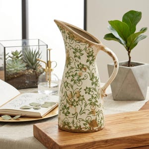 May include: A white ceramic mug with a black handle and the text "But First, Coffee" in a bold, black font. The mug is set against a blurred background, suggesting a cozy setting. The mug appears to be approximately 4 inches tall.