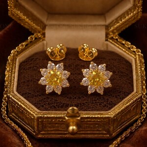 Könnte beinhalten: Ein Paar goldene Ohrstecker in Blumenform, jeweils mit einem zentralen runden gelben Edelstein, der von einem Kranz aus kleinen, klaren weißen Steinen umgeben ist. Die Ohrringe werden mit passenden goldenen Schmetterlingsverschlüssen geliefert.