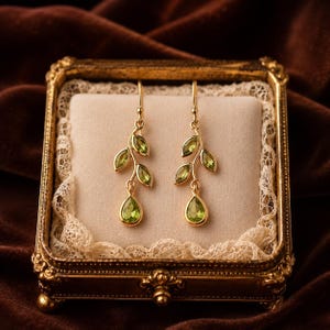 May include: A pair of gold drop earrings featuring a branch-like design with multiple marquise-cut green peridot stones and a single pear-cut green peridot stone at the base of each earring, suspended from simple gold ear wires.