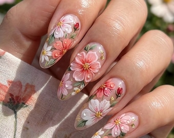 May include: Close-up of long, almond-shaped nails with intricate floral designs. The nails display pink, white, and red flowers with green leaves, gold accents, and water droplet details. The overall effect is delicate and artistic.