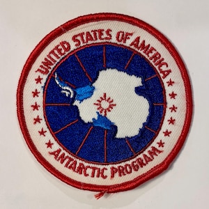 May include: Embroidered patch featuring the words "UNITED STATES OF AMERICA ANTARCTIC PROGRAM" in red and white. The patch has a circular design with a blue background and a white continent shape in the center.