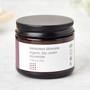 Peut inclure: Un pot en verre brun avec un couvercle noir contenant une crème de jour bio pour peau mature, de la marque Conscious Skincare.