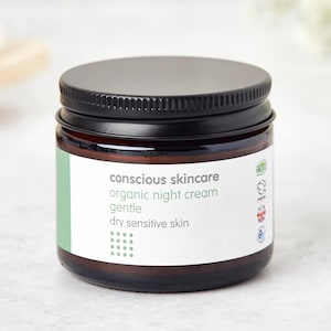 May include: A brown glass jar with a black lid containing a white label that reads "conscious skincare organic night cream gentle dry sensitive skin". The label also features several green and white certification logos.