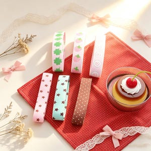 May include: An assortment of decorative ribbons in various colors and patterns, including stars, polka dots, strawberries, and clovers. A red polka-dot napkin and a dessert with a cherry on top are also present.